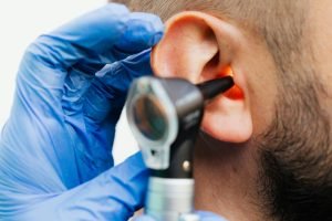 Gros plan d'un médecin utilisant un otoscope pour examiner l'oreille d'un patient dans un contexte clinique.