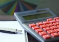 Calculatrice avec boutons rouges, stylo et feuille sur une table
