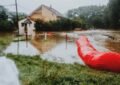 Rue inondée devant une maison, tube rouge et herbe mouillée