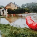 Rue inondée devant une maison, tube rouge et herbe mouillée