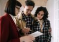 Trois individus consultent attentivement un papier, une note prise, dans un espace domestique
