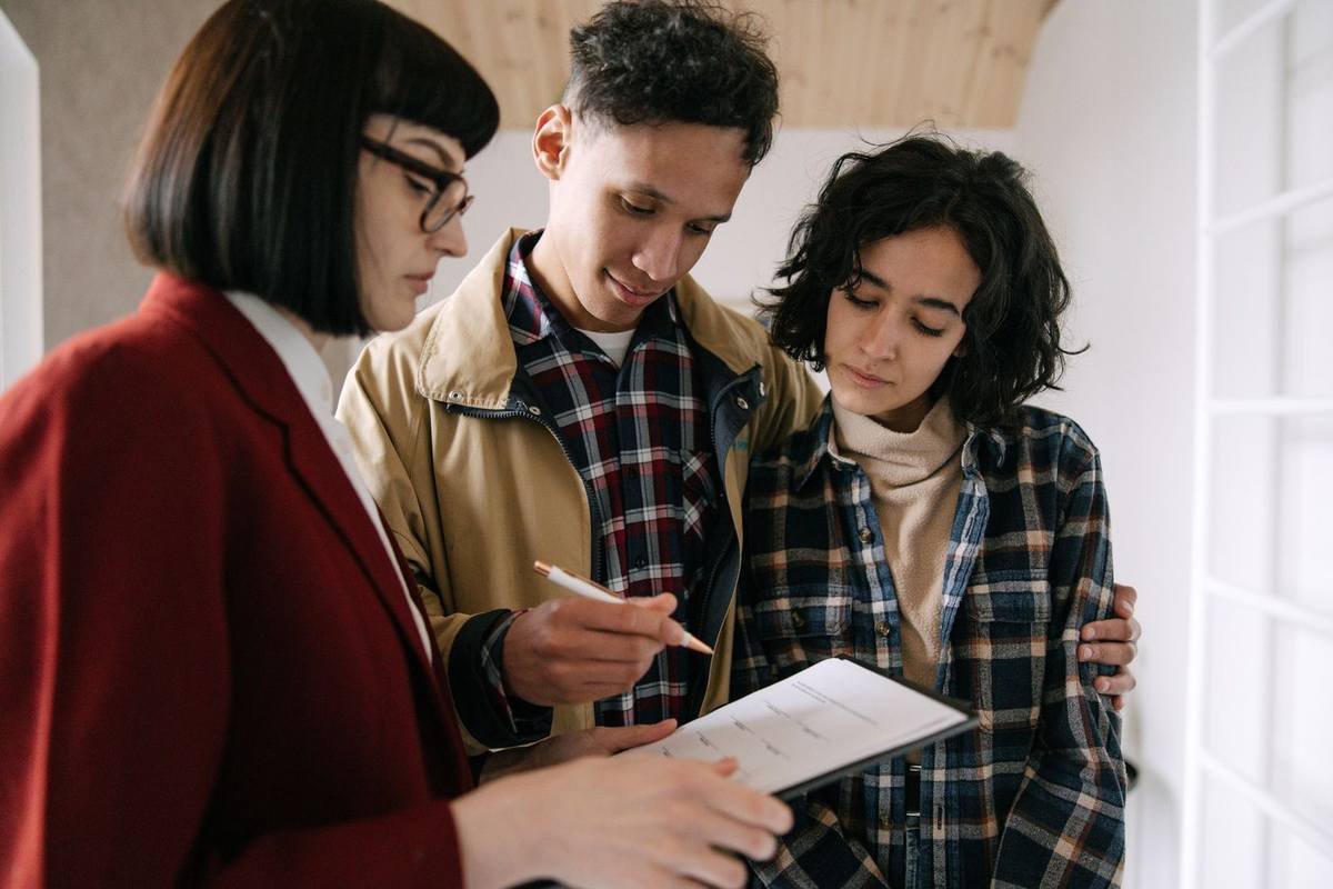 Trois individus consultent attentivement un papier, une note prise, dans un espace domestique