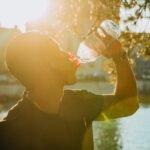 Un homme en silhouette boit de l'eau au bord d'un fleuve ensoleillé