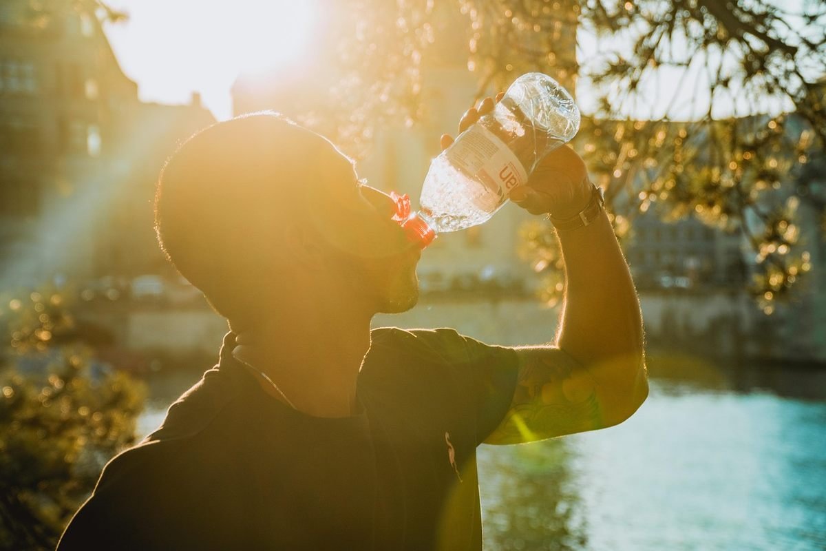 Un homme en silhouette boit de l'eau au bord d'un fleuve ensoleillé