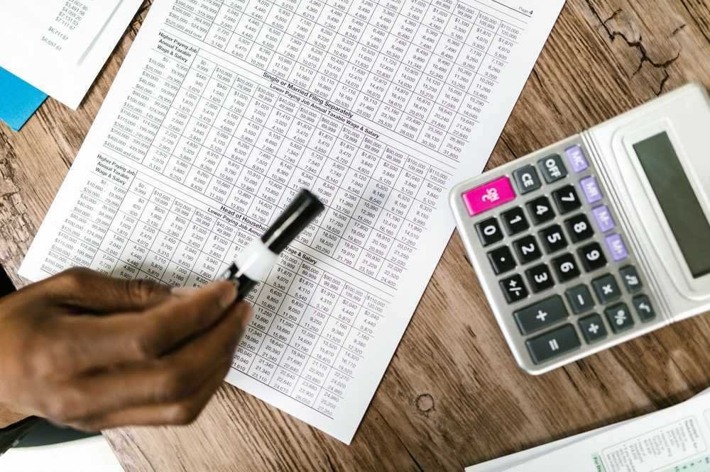 Une main écrit sur un tableau de chiffres avec une calculatrice Une main écrit sur un tableau de chiffres avec une calculatrice